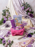 Royal Treatment Mini Spa Gift Set in pink bow headband basket with Spa Scentiale hydrogel eye and lip duo, Wonderful body lotion, gold shimmer mist and bath bomb surrounded by purple roses and amethyst crystals